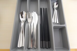 Un plateau gris, divisé en compartiments, contenant divers ustensiles, notamment des cuillères, des fourchettes et des baguettes.