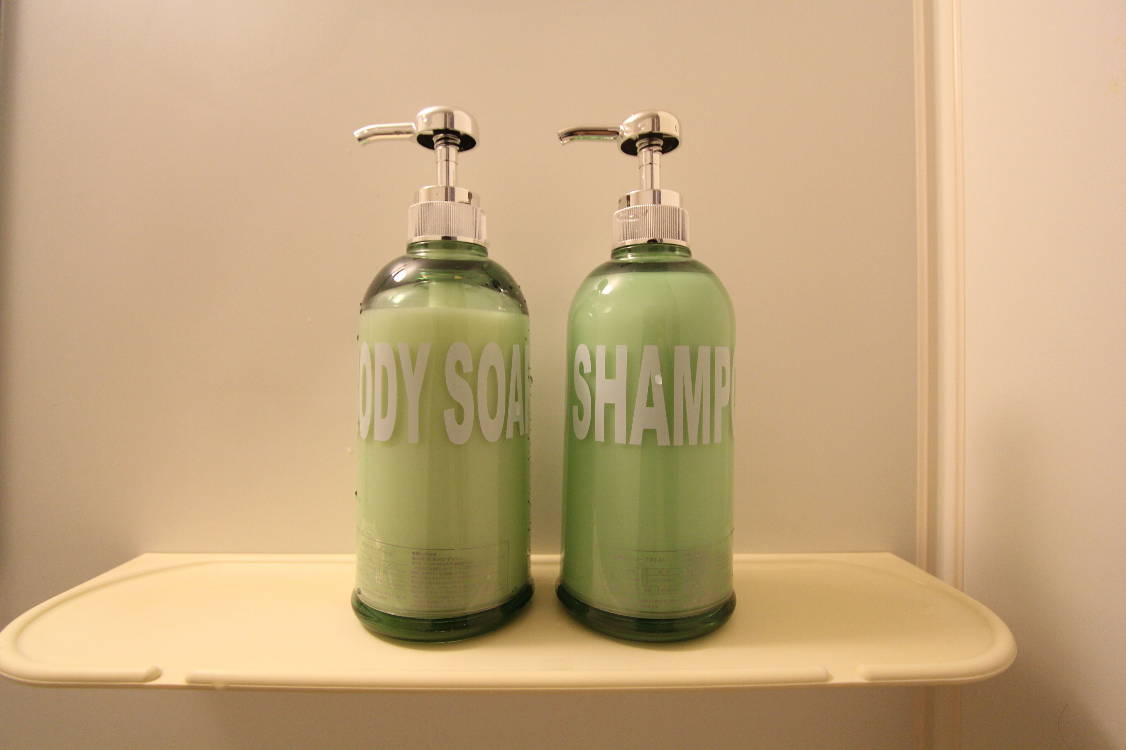 Zwei grüne Flaschen mit Duschseife und Shampoo auf einem weißen Regal.