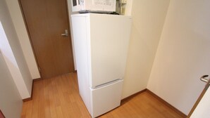 A small kitchen with a white refrigerator, wooden flooring, and a closed door. - Cozy Stay in Nakano Honcho - 7min to Shin-Nakano, 2 Stops to Shinjuku(33) (中野区本町)