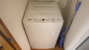 A compact, white washing machine in a corner of a room with wooden flooring and a white wall. - Cozy Stay in Nakano Honcho - 7min to Shin-Nakano, 2 Stops to Shinjuku(33) (中野区本町)