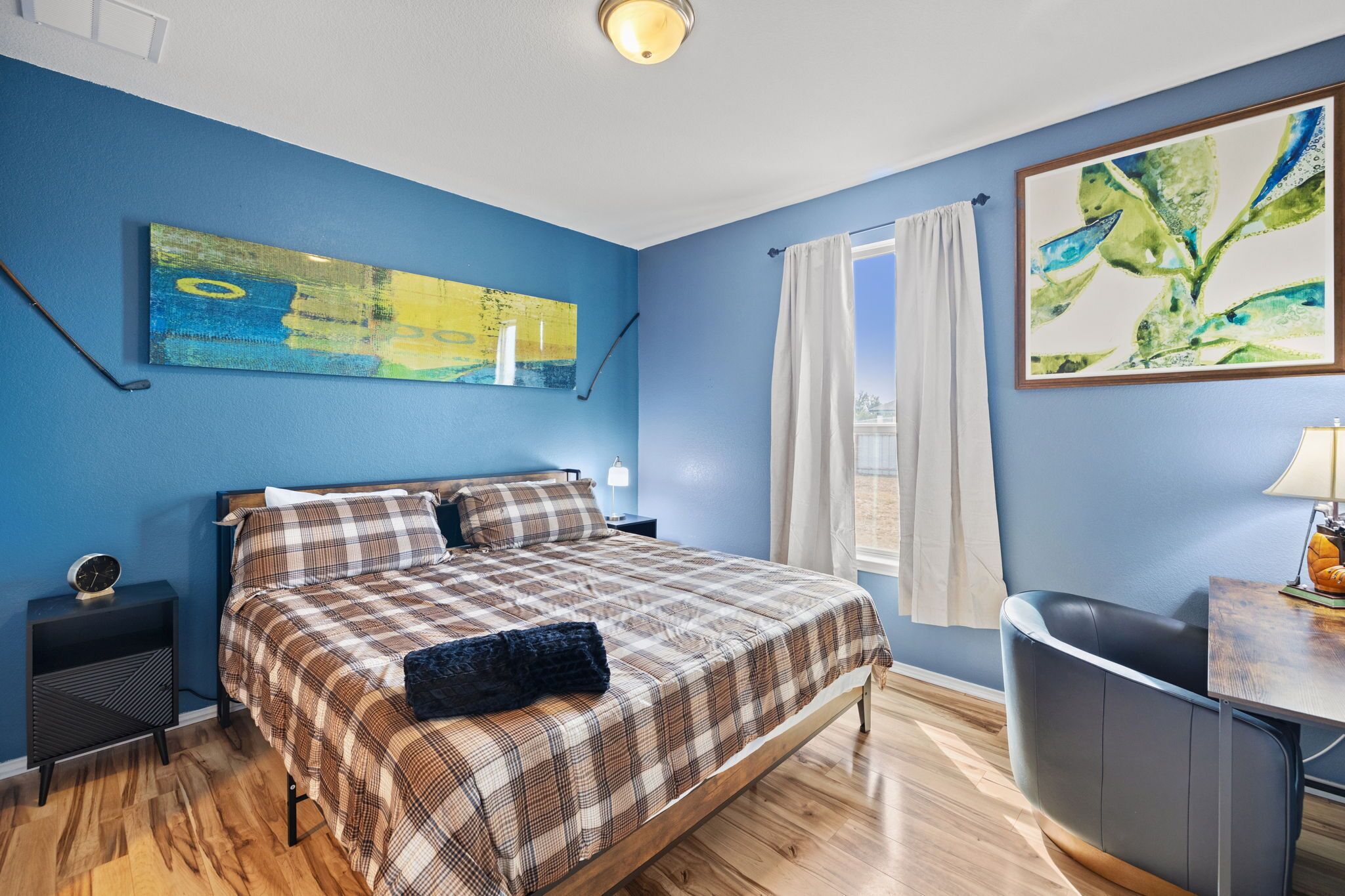 A bedroom with a bed, a nightstand, a lamp, a desk, and a chair.