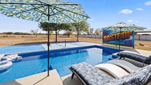 A swimming pool with lounge chairs and an umbrella, surrounded by a fenced area with trees. - 5 BR King Size Beds Pickleball, Pool 25 mi to COTA (Bastrop)