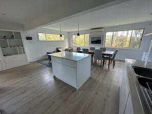 A modern kitchen with a central island, dining area with chairs, and large windows.