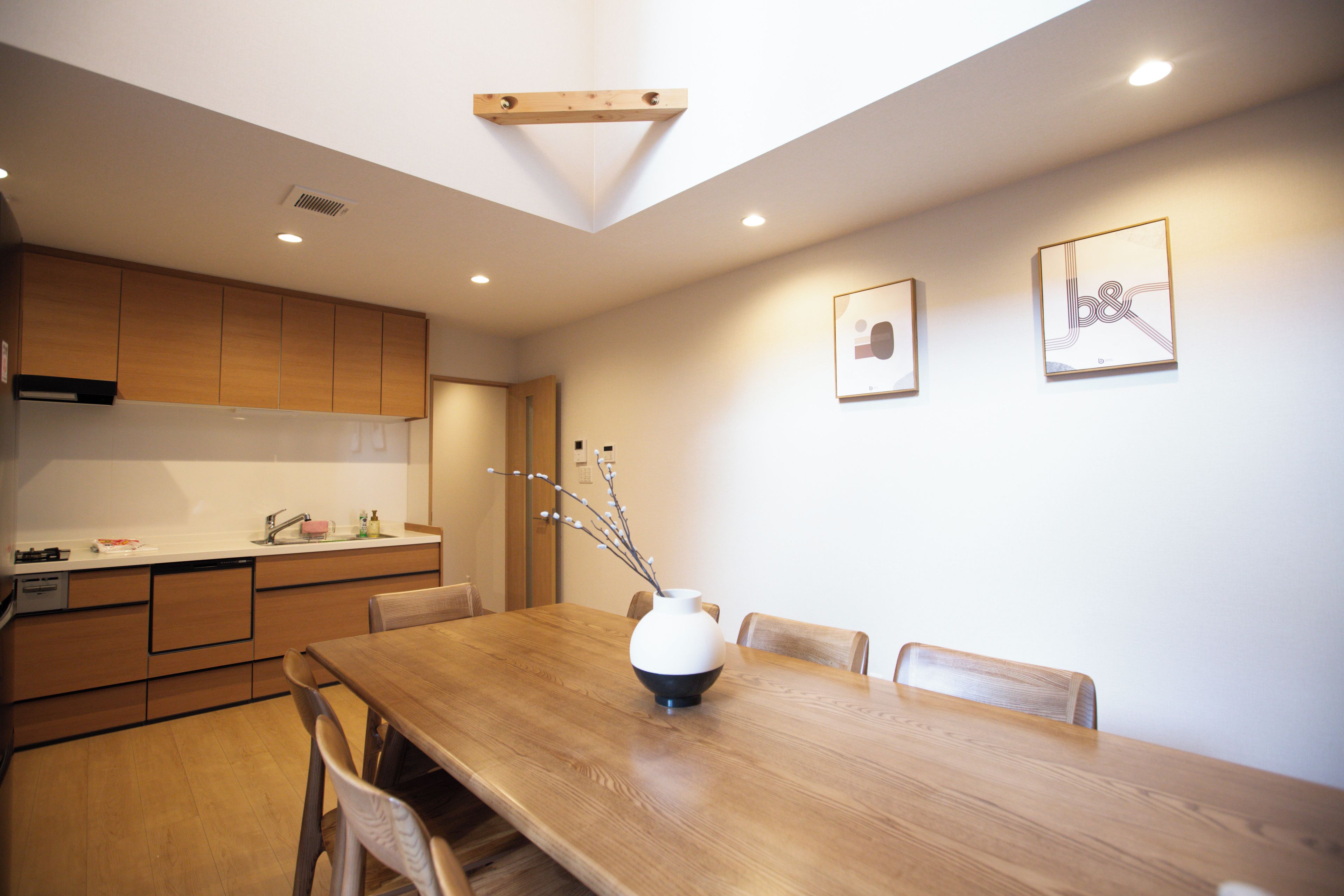 A modern kitchen with wooden cabinets, a dining table, and chairs. There is a vase with branches on the table.