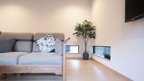 Un salon moderne avec un canapé gris, une table basse en bois, une plante en pot et un téléviseur fixé au mur.