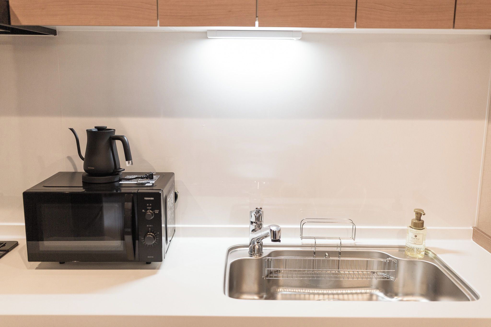 Una cucina compatta con microonde, bollitore, lavello e dispenser per sapone.