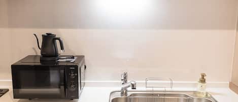 Cocina compacta con microondas, hervidor, lavabo y dispensador de jabón.