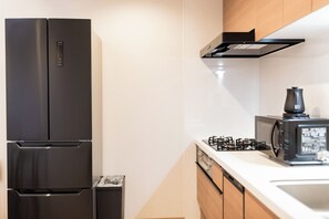 A modern kitchen with a black refrigerator, a microwave, and a gas stove. - b&FLAT-Hanazono (Osaka)
