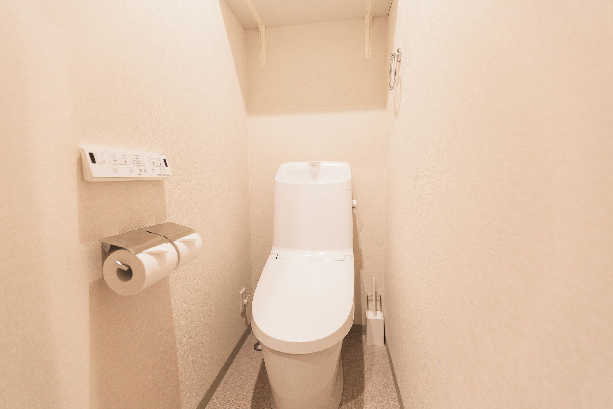 A small, modern bathroom with a toilet, a toilet paper holder, and a flush handle.