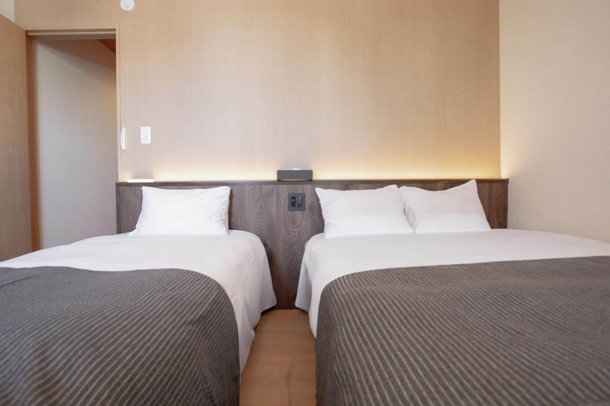 A hotel room with two beds, a wooden headboard, and a bedside table with a lamp.
