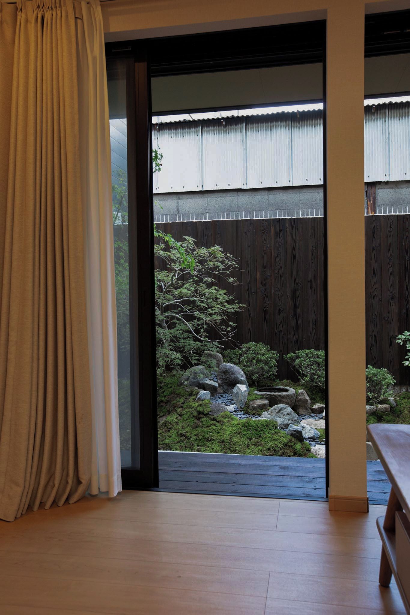 A room with a sliding glass door leading to a garden with a wooden fence, rocks, and greenery.