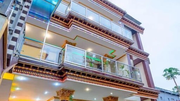 A multi-story hotel with a modern design, featuring balconies, a central courtyard with potted plants, and a staircase leading to the upper levels.