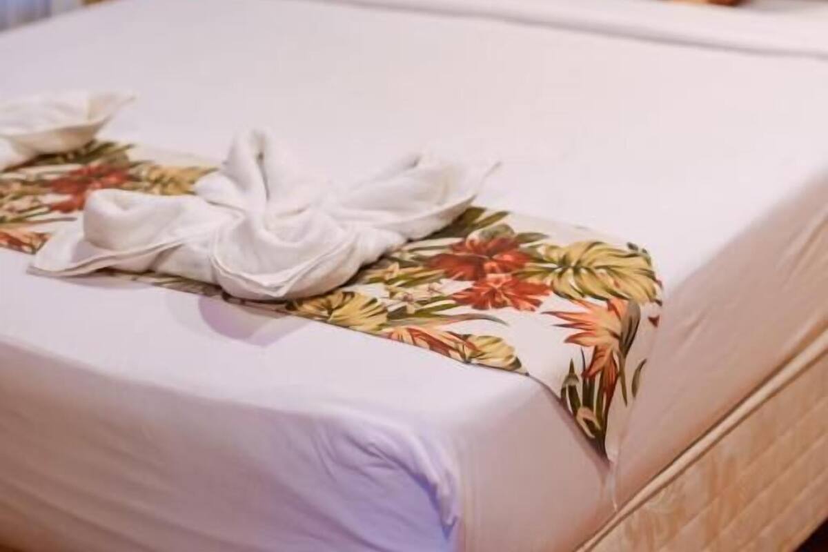 Una cama bien hecha con ropa de cama floral y una toalla blanca a un lado.
