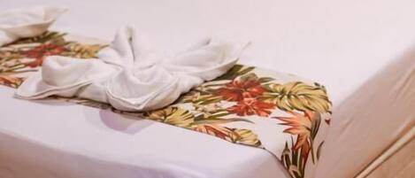 A neatly made bed with floral bedding and a white towel on the side.