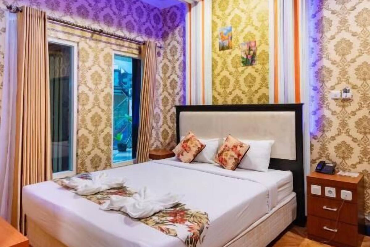 Un dormitorio con una cama grande, una mesita de noche y una ventana con cortinas.