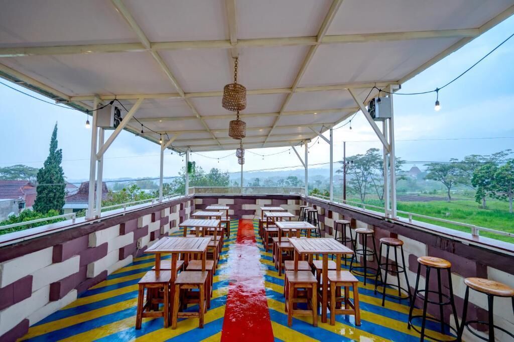 An outdoor covered dining area with wooden tables and chairs, a colorful floor, and a view of the countryside.