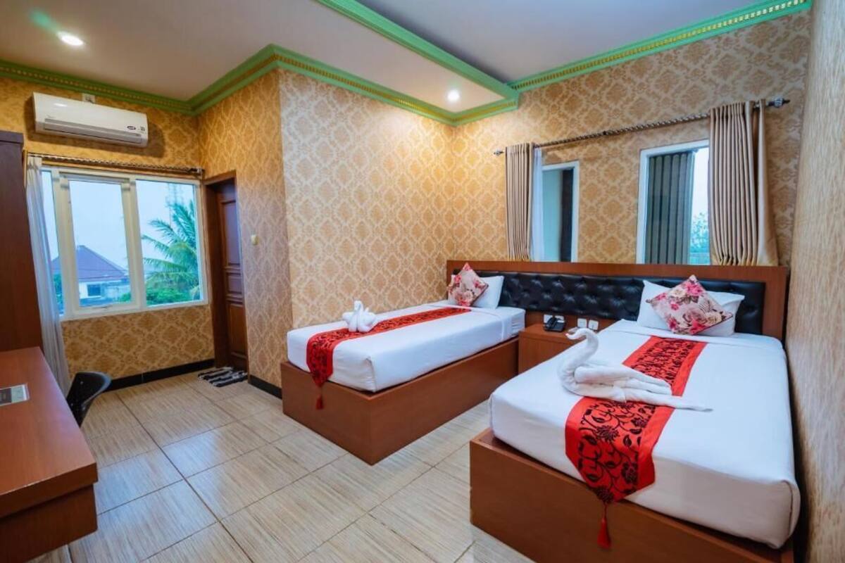 Habitación de hotel con dos camas, un escritorio y una ventana con vista a palmeras.