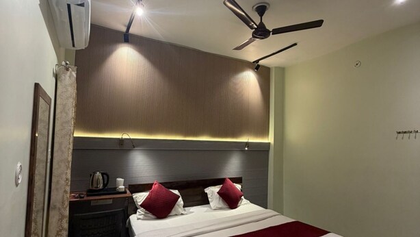 A hotel room with a bed, a desk, a chair, a ceiling fan, and an air conditioning unit. - Jogi Lodge (Varanasi)