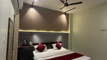 A hotel room with a bed, a desk, a chair, a ceiling fan, and an air conditioning unit.