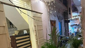 A narrow alleyway with a small step leading to a door, a yellow trash bin, and potted plants. - Jogi Lodge (Varanasi)