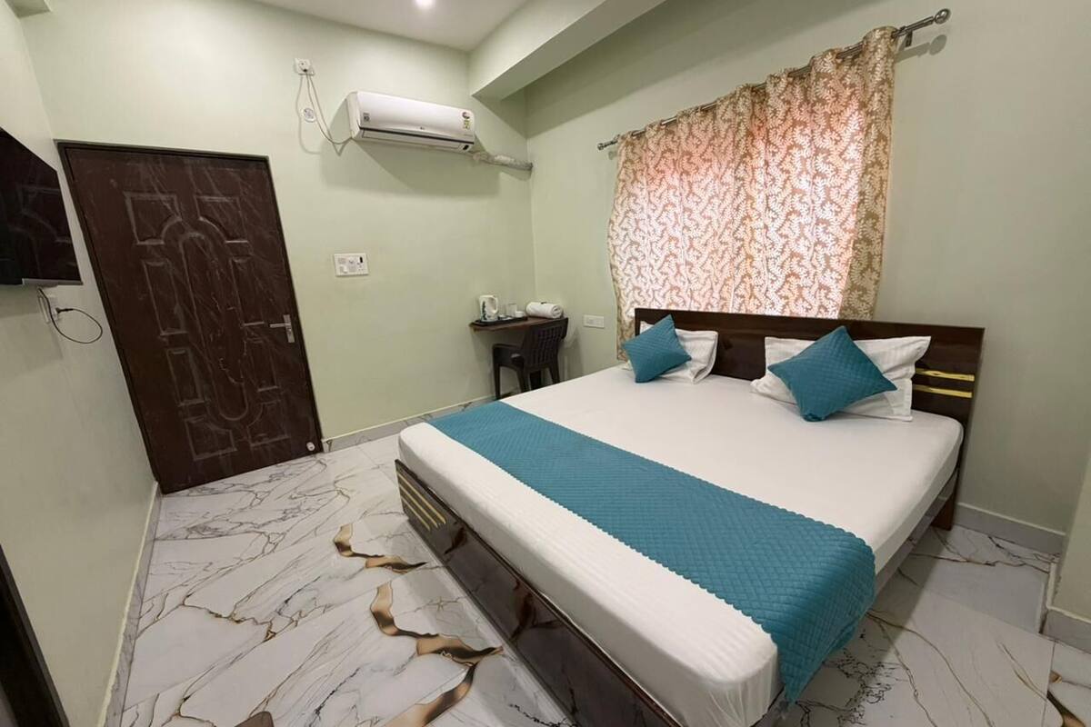 A bedroom with a bed, a desk, an air conditioner, and a door.