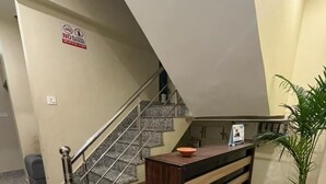 A hotel lobby with a marble floor, a reception desk, a staircase, and a 'No Alcohol Smoking' sign. - Jogi Lodge (Varanasi)