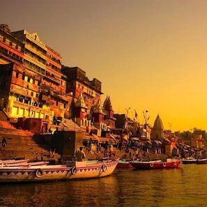 A riverside scene with boats and buildings along the water. - Jogi Lodge (Varanasi)
