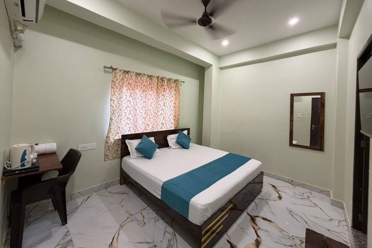 A bedroom with a bed, a desk, a chair, a ceiling fan, and a window with curtains.
