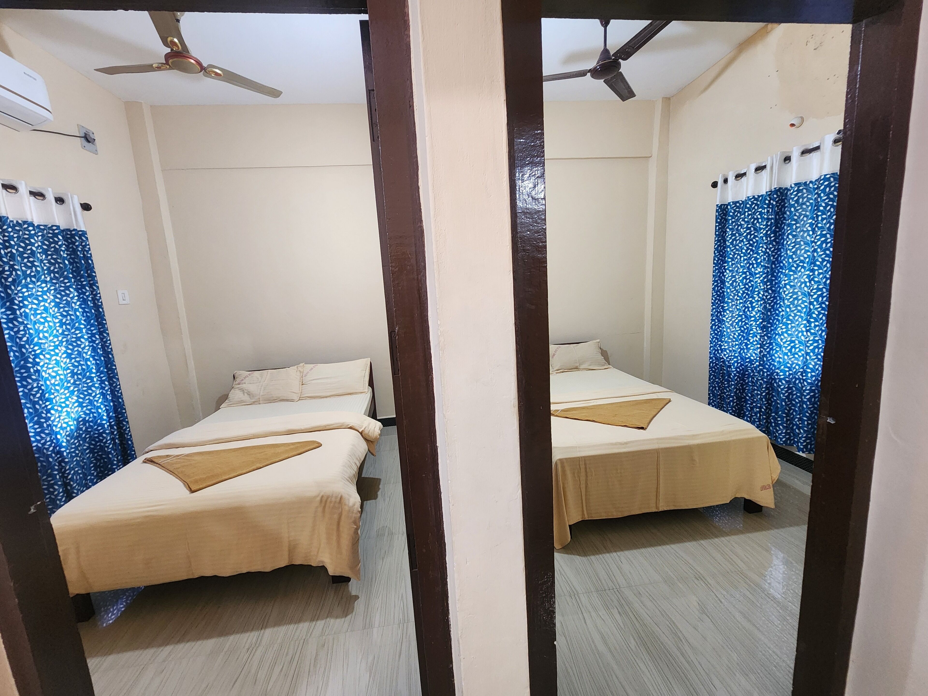 A mirrored view of a bedroom with two beds, a ceiling fan, and patterned curtains.
