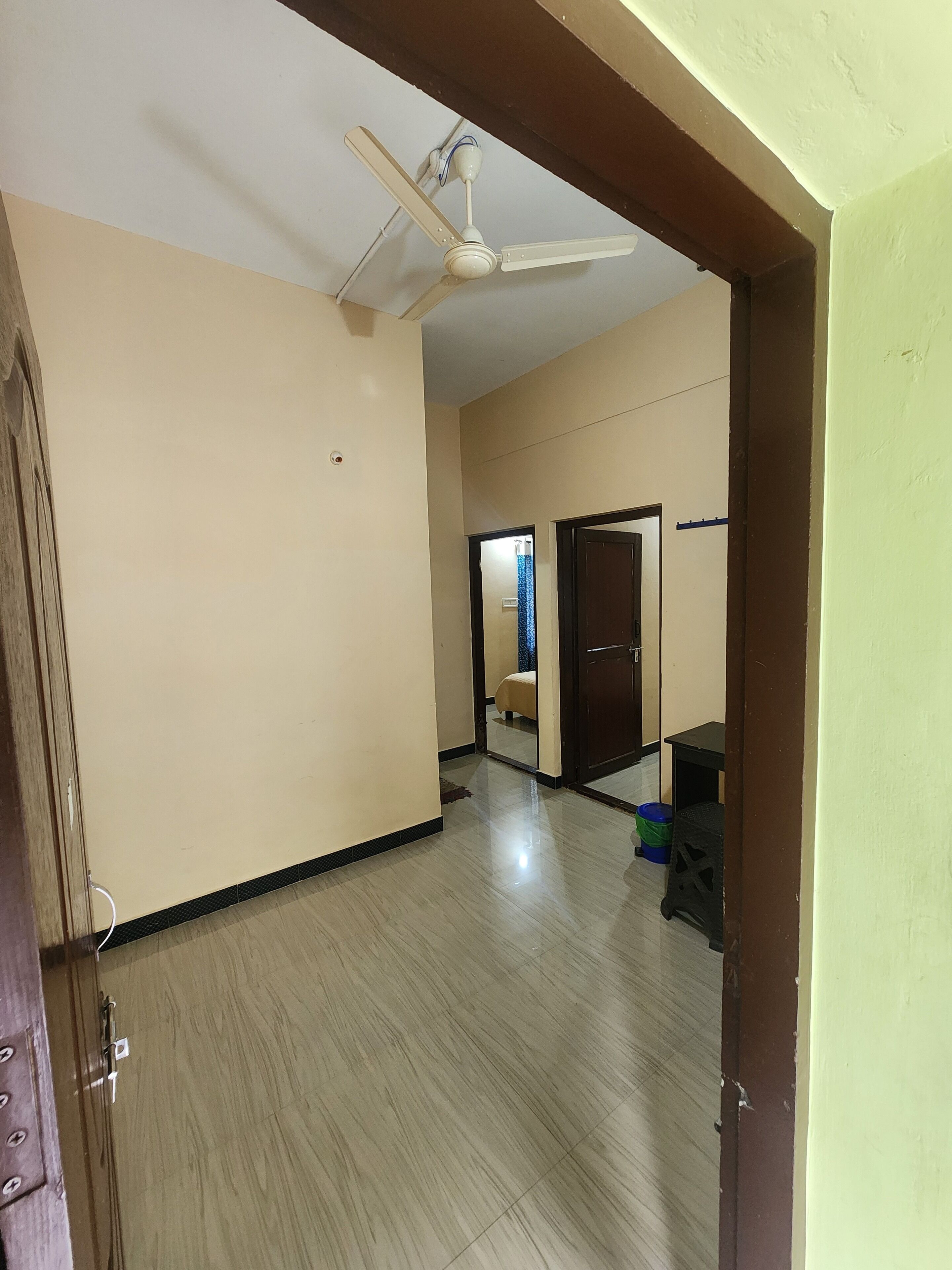 A hallway with a ceiling fan, a door, and a small table with a trash bin.