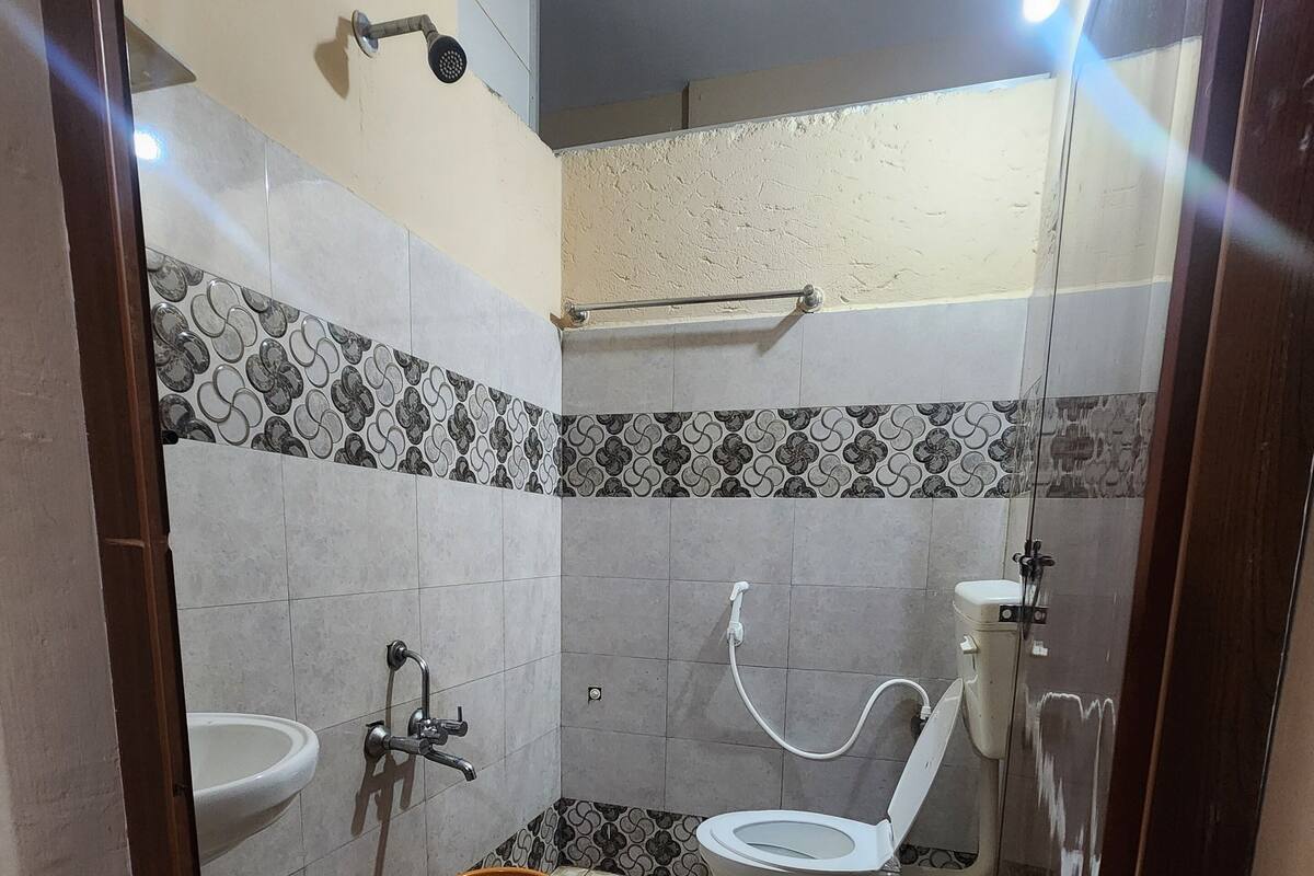 A bathroom with a toilet, sink, shower, patterned tiles, and a bucket.