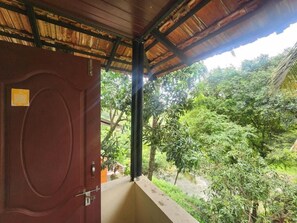 A wooden door with a metal handle, leading to a balcony with a view of lush greenery and a river. - Siruvani River Retreat (Mannarkkad)