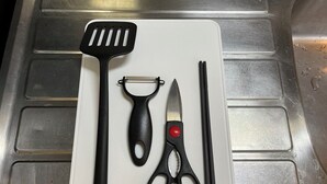 Un évier de cuisine sur lequel est posée une planche à découper blanche, servant de support à divers ustensiles de cuisine.