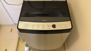 Une machine à laver Haier dotée d’un panneau de commande, d’un tuyau d’arrivée d’eau et d’un tuyau d’évacuation.