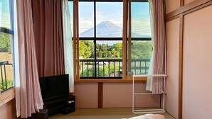 Een kamer met een bed, een televisie, een raam met uitzicht op een berg en een balkon.