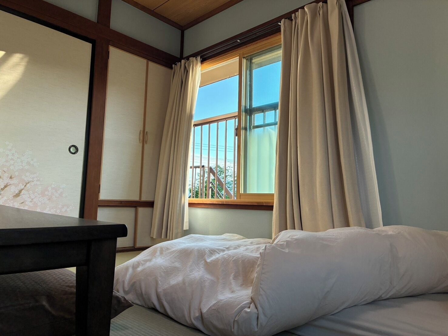 A room with a bed, a window with curtains, a wooden table, and a sliding door with a floral design.
