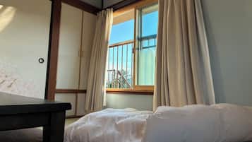 A room with a bed, a window with curtains, a wooden table, and a sliding door with a floral design.