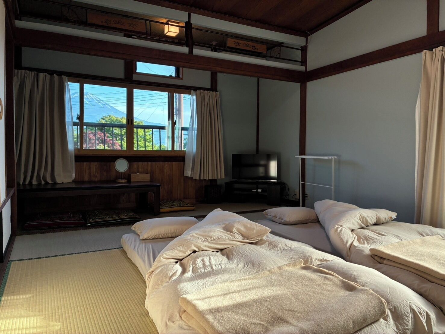 Una habitación de estilo japonés tradicional con suelo de tatami, una cama futón, un televisor y una ventana con cortinas.