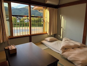 A room with a bed, a table, and a window with a view of a mountain. - Crab and Wagyu Beef Fujisan-tei (Fujikawaguchiko)