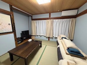 A room with a wooden ceiling, a TV on a stand, a sofa with cushions, a table, and a window with curtains. - Crab and Wagyu Beef Fujisan-tei (Fujikawaguchiko)