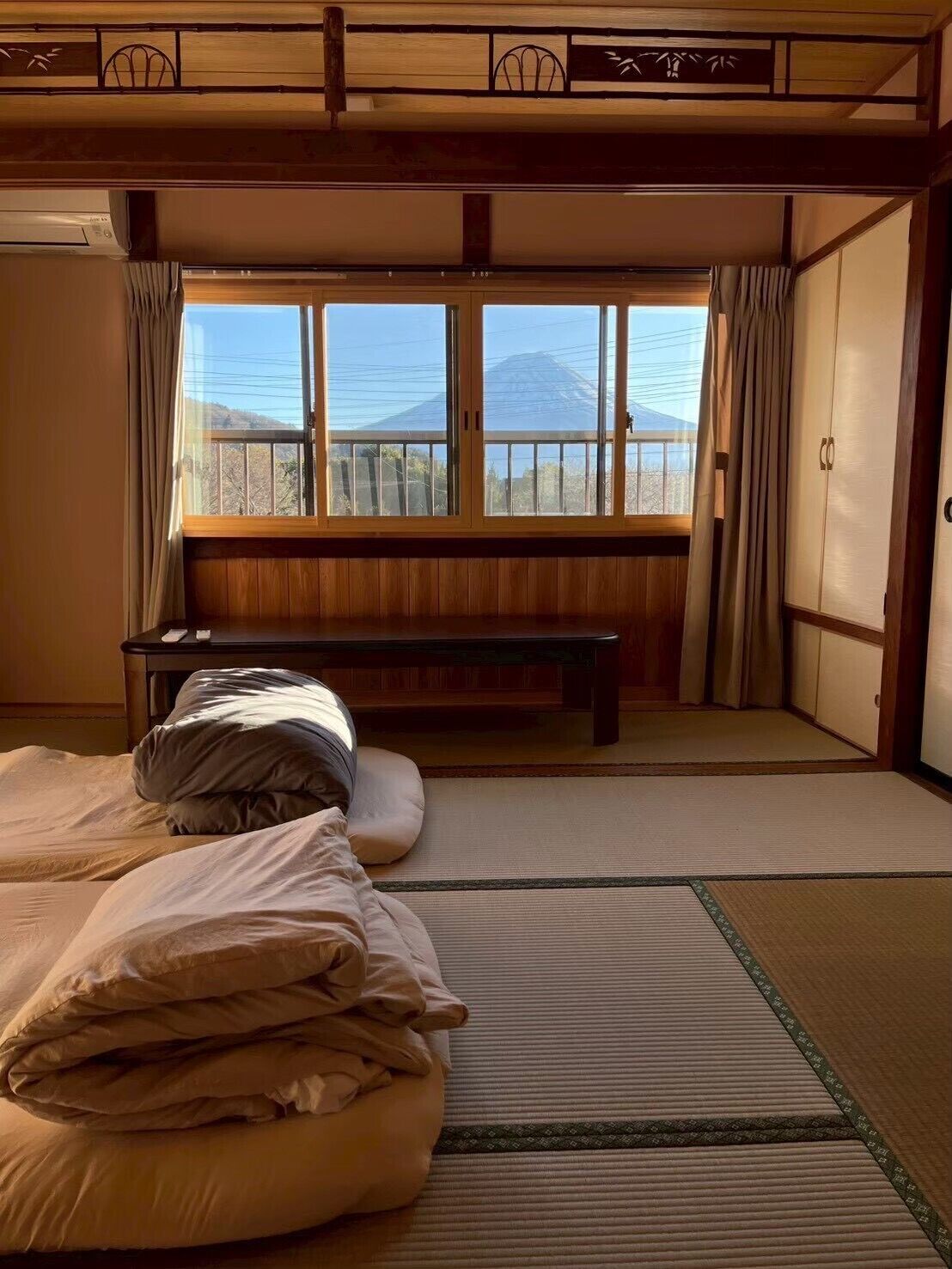 Um quarto japonês tradicional com tatames, um futon, um banco de madeira e vista para uma montanha.