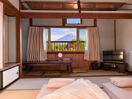 A traditional Japanese-style room with tatami flooring, a futon bed, a television, and a view of greenery outside.