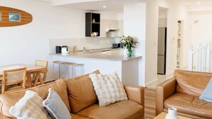 A modern living space with a kitchen, a dining area, and two leather sofas. - Beachfront Apartment | Pool, Tennis & Parking (Newcastle East)