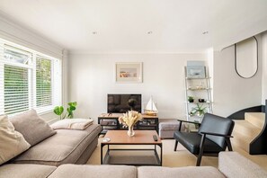Un salon moderne avec un canapé, une table basse, un fauteuil noir et un téléviseur.