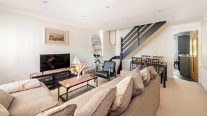 Un salon moderne avec un canapé, une table basse et un téléviseur. Un escalier avec une rampe mène à une autre pièce.