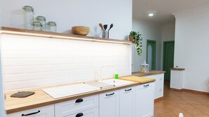 A kitchen with white cabinets, a wooden countertop, and a backsplash. There is a mat on the floor and a chair in the corner. - House Marisa (Casoria)