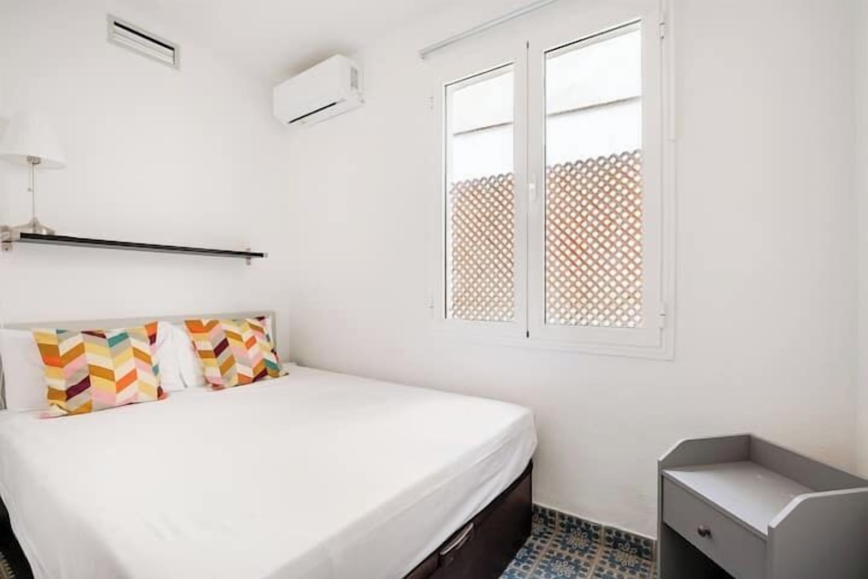 A bedroom with a bed, a bedside table, and a window with a lattice screen.