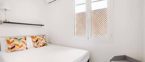 A bedroom with a bed, a bedside table, and a window with a lattice screen.
