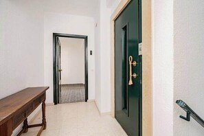 A hallway with a wooden bench, a dark green door with a brass handle, and a white textured wall. - Boutique Abades Apartment I (Seville)