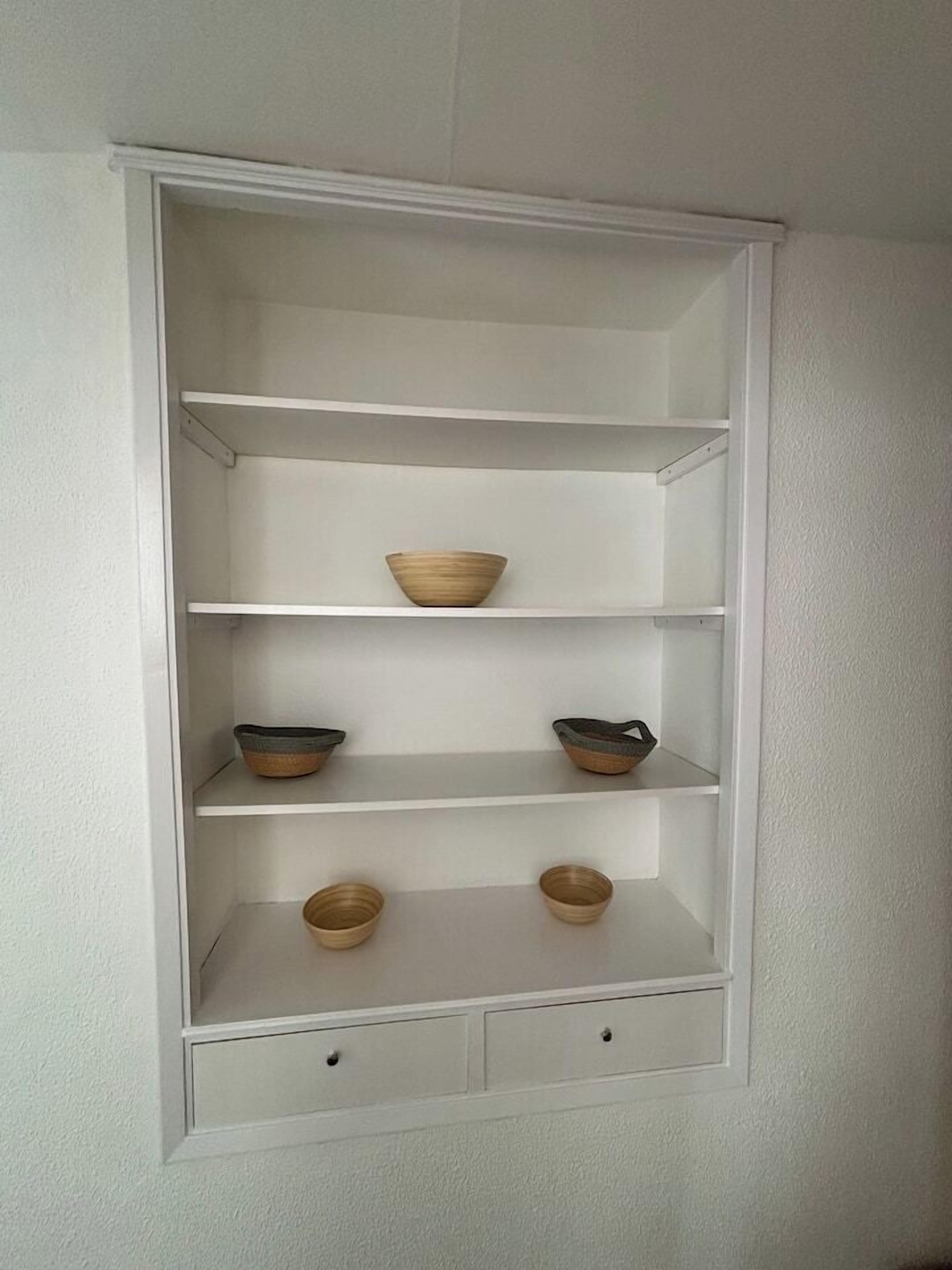 Ein weißes Regalsystem mit vier Ablagen und zwei Schubladen, in denen verschiedene Schalen aufbewahrt werden.